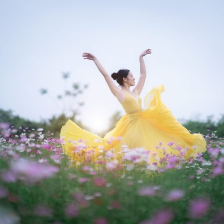 Donna in abito giallo che danza libera in un prato fiorito, simbolo di riscatto, vitalità e piena armonia con il proprio